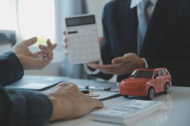 El vendedor de automóviles o el gerente de ventas de los hombres asiáticos de primer plano se ofrece a vender un automóvil y explica y lee los términos de la firma de un contrato de automóvil y un seguro