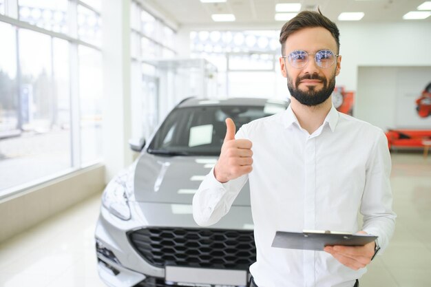 Vendedor de autos amigable sonriente de pie en el salón de autos