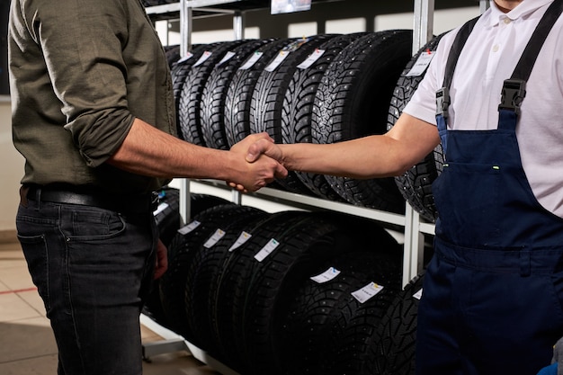 Vendedor y cliente dándose la mano en el taller de servicio automático, el hombre tomó la decisión, comprando neumáticos de coche para el invierno