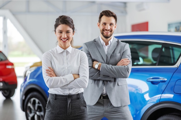 Foto vendedor de coches amistoso sonriente de pie en el salón del coche con los brazos cruzados. siempre es un placer para ambas partes comprar un automóvil en el lugar correcto.