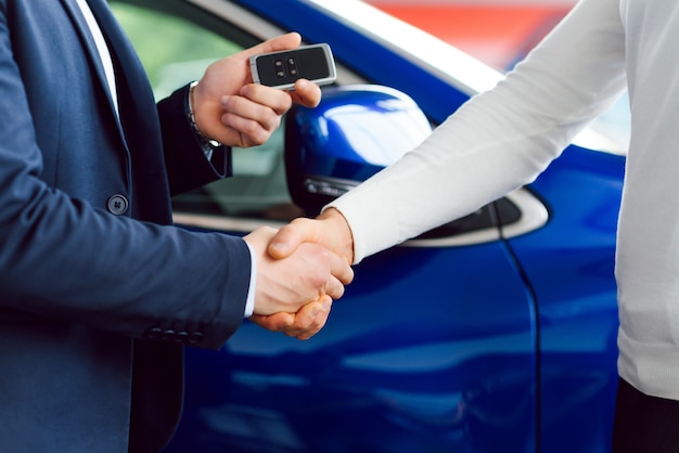 Vendedor de coches entregando las llaves de un coche nuevo a un joven empresario