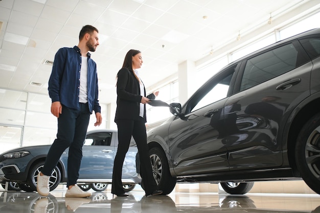 Un vendedor de coches sonriente de pie en el salón de automóviles con el cliente y mostrando los coches en venta