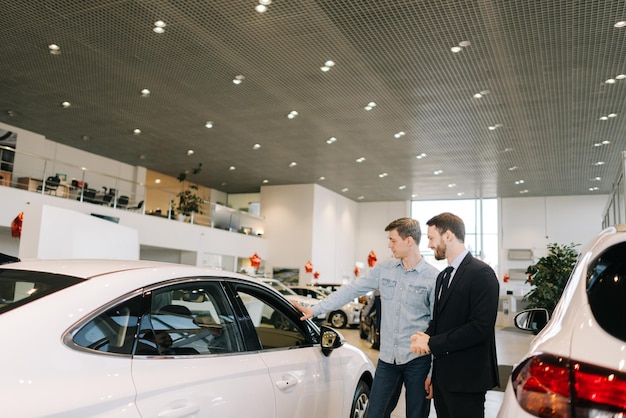 Vendedor confiado con traje de negocios que muestra un nuevo comprador interesado en un automóvil en un concesionario de automóviles. Concepto de elección y compra de autos nuevos en la sala de exposición