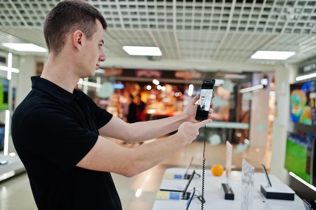 Foto vendedor, consultor profesional de teléfonos móviles en una tienda de tecnología o en una tienda, sostenga un nuevo teléfono inteligente a mano y haga selfie con la cámara