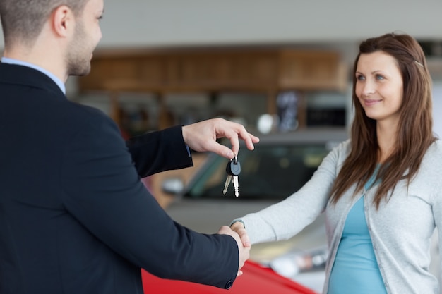 Vendedor dando las llaves del coche mientras agita la mano de una mujer