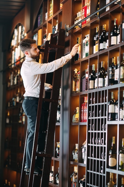 Vendedor de bebidas alcoólicas classifica garrafas em pé na escada