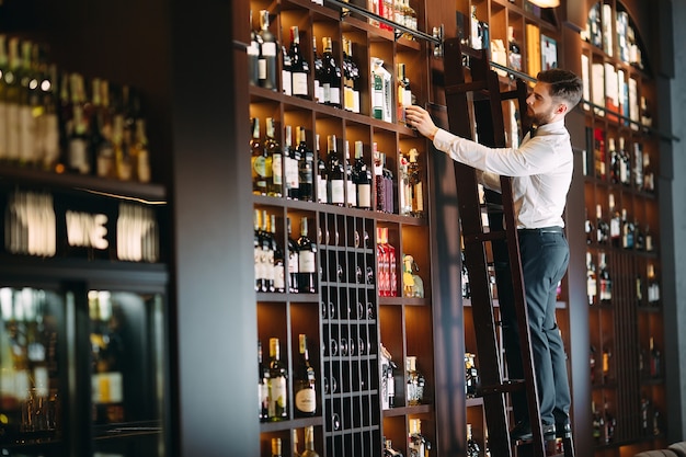 Foto vendedor de bebidas alcoólicas classifica garrafas em pé na escada