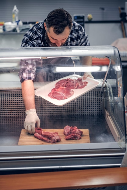 Vendedor de carne barbudo vestido com uma camisa de lã servindo carne fresca cortada em um mercado.