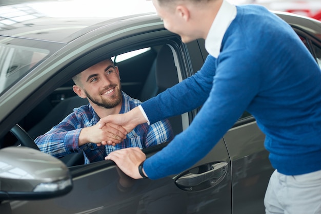 Vendedor de carro e aperto de mão do cliente na concessionária.