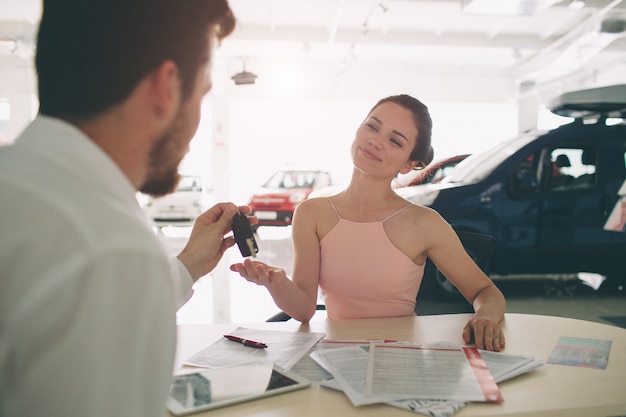 Vendedor de carros amigável conversando com uma jovem mulher e mostrando um carro novo dentro da sala de exposições