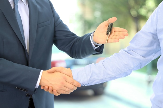 Vendedor de carros entregando as chaves de um carro novo a um jovem empresário