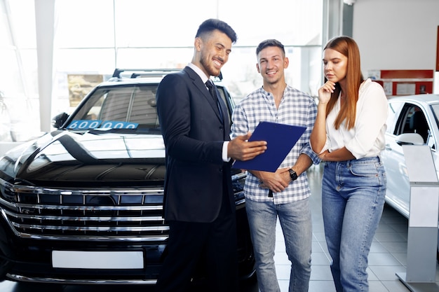 Vendedor de carros falando sobre as características do carro novo para o casal na concessionária