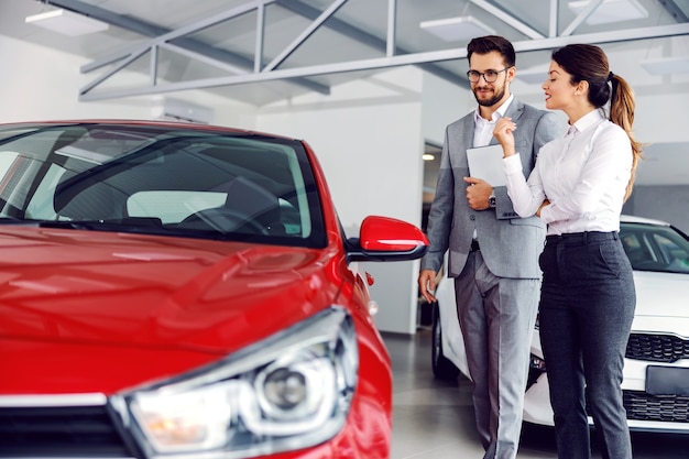 Foto vendedor de carros sorridente no salão do carro com o cliente e mostrando os carros à venda.