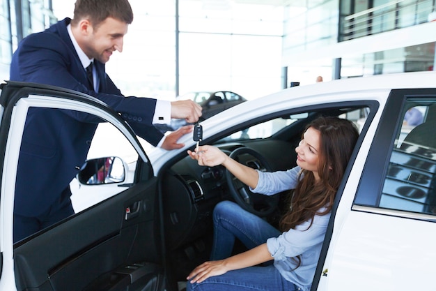 Vendedor de carros vende um carro para um cliente satisfeito na concessionária e entrega as chaves