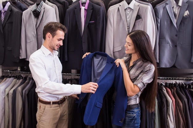 Vendedor de menina ajuda a pegar um cliente em uma boutique de roupas masculinas de jaqueta