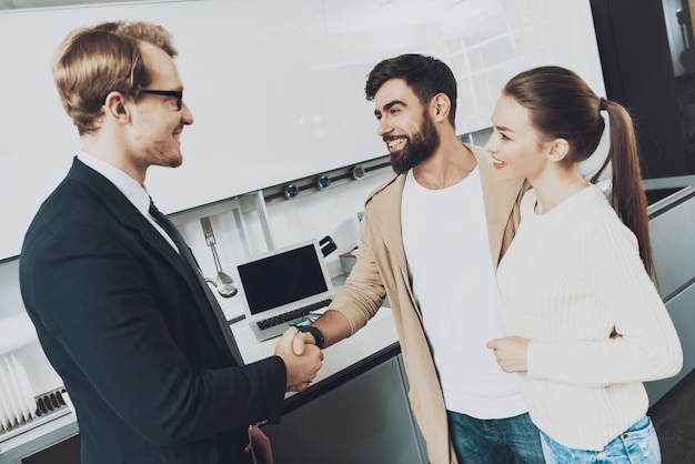 Vendedor e cliente com a esposa estão apertando as mãos na cozinha