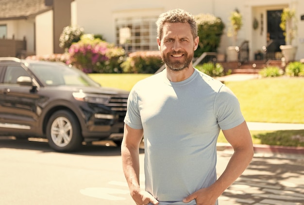 Vendedor feliz que presenta la casa del suburbio y el corredor de coches