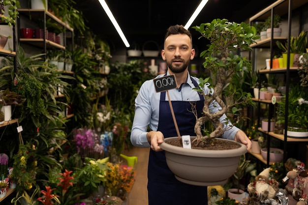 Vendedor de floristería con bonsai en sus manos contra el fondo de plantas en macetas de flores