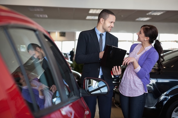 Vendedor hablando con una mujer sonriente al lado de un coche