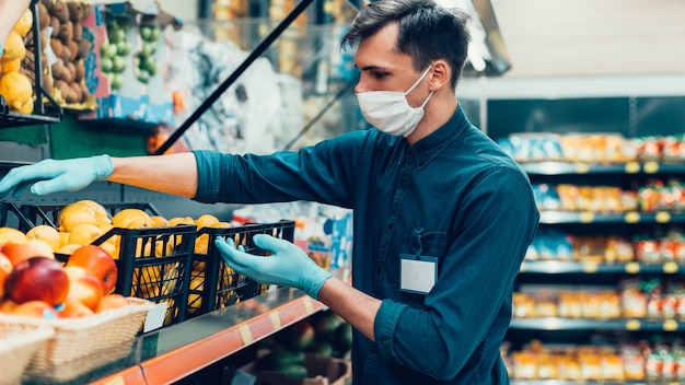 Vendedor con una máscara protectora de pie frente al mostrador con fruta. coronavirus en la ciudad