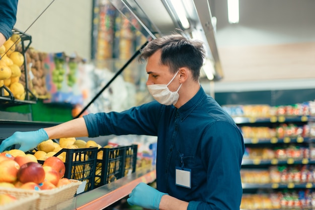 Vendedor con una máscara protectora de pie frente al mostrador con fruta. coronavirus en la ciudad