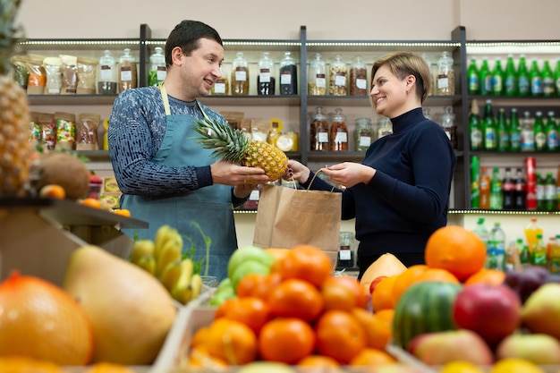 Vendedor masculino pasa una bolsa artesanal de comestibles a una clienta