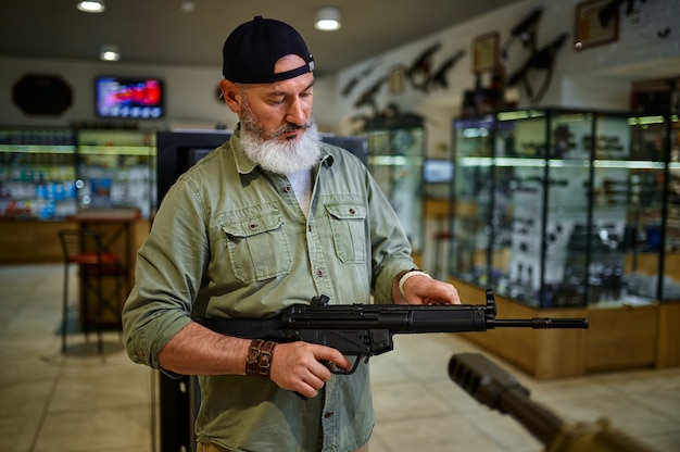 Vendedor masculino tiene rifle automático en la tienda de armas. Interior de la tienda de armas, surtido de municiones y municiones, elección de armas de fuego, pasatiempo y estilo de vida de tiro, autoprotección