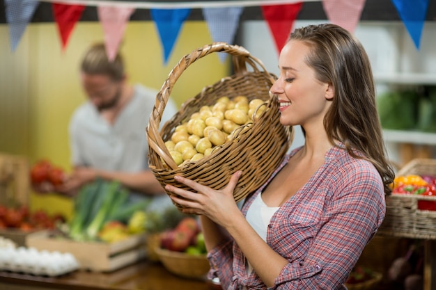 Vendedor mujer sosteniendo una canasta si las papas en la tienda de comestibles