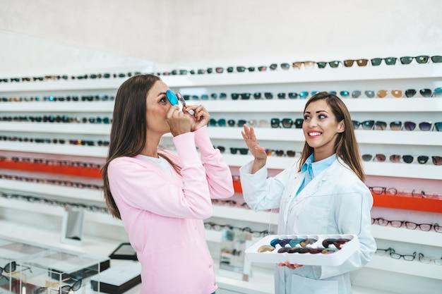 Vendedor de mujeres de mediana edad y cliente eligiendo anteojos nuevos en la moderna tienda óptica. Concepto de compras.