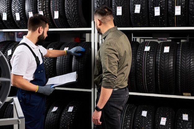 El vendedor ofrece nuevas llantas de goma, neumáticos y llantas para el automóvil. El cliente masculino vino a realizar una compra en el taller de servicio de automóviles. Mecánico automotriz mostrando surtido de neumáticos.