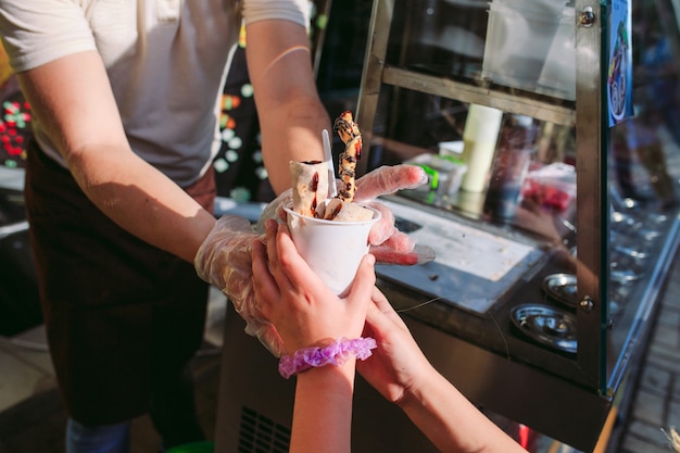 El vendedor le pasa el helado a una niña. rollos de helado salteados en una sartén de congelación. Helado laminado orgánico natural, postre hecho a mano.