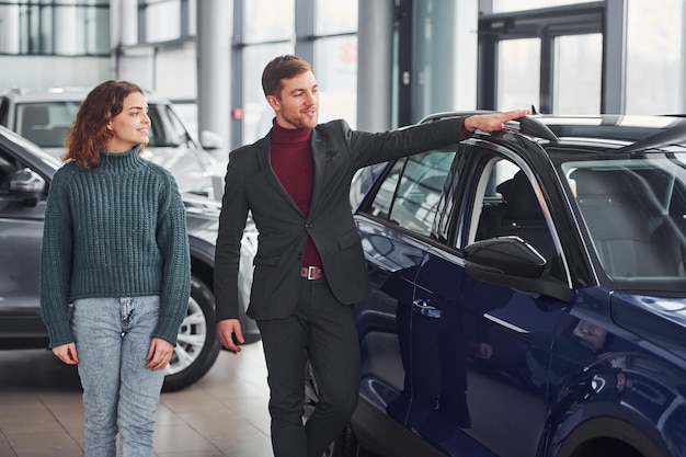 Vendedor profesional que ayuda a la joven a elegir un nuevo automóvil moderno en el interior.