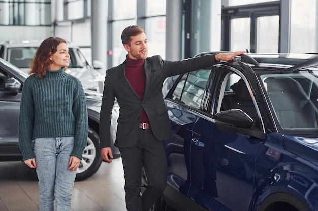 Vendedor profissional ajudando jovem escolhendo novo automóvel moderno dentro de casa.