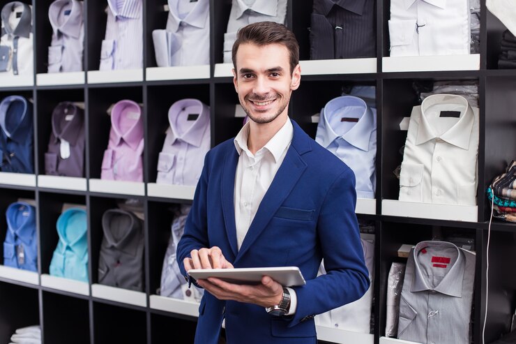 Vendedor de ropa masculina boutique trabajando en una tableta en el fondo de pie con camisas