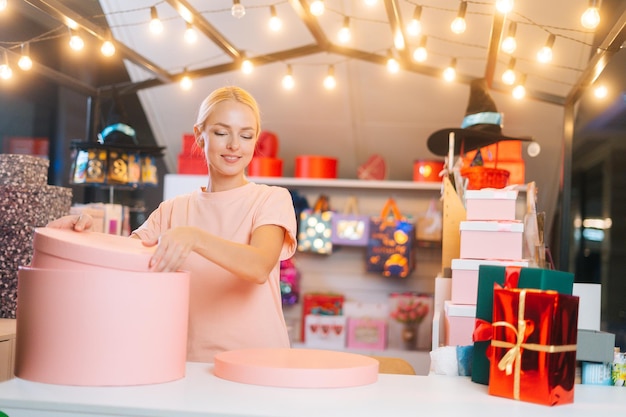 Vendedor de sexo femenino alegre atractivo que clasifica las cajas del día de fiesta que se colocan detrás del mostrador de la tienda preparando ...