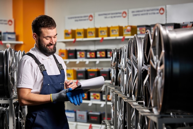 Vendedor de sexo masculino en la tienda de automóviles tomando notas, verificando el documento y examinando las características, mirando el estante con llantas automáticas