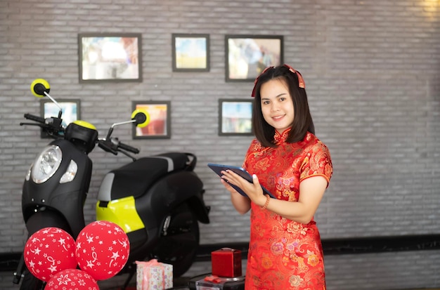 Vendedor sosteniendo una tableta móvil trabajando en un concesionario de motocicletas en la sala de exposición Vendedores vestidos con cheongsams chinos tradicionales para el Año Nuevo Chino