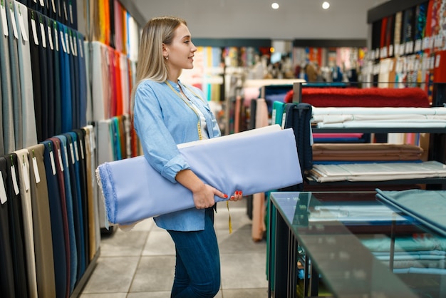 El vendedor tiene pila de tela en la tienda textil. Estante con paño para coser