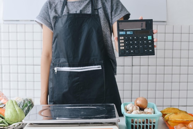 Vendedor vestindo avental e mostrando calculadora na câmera no mercado