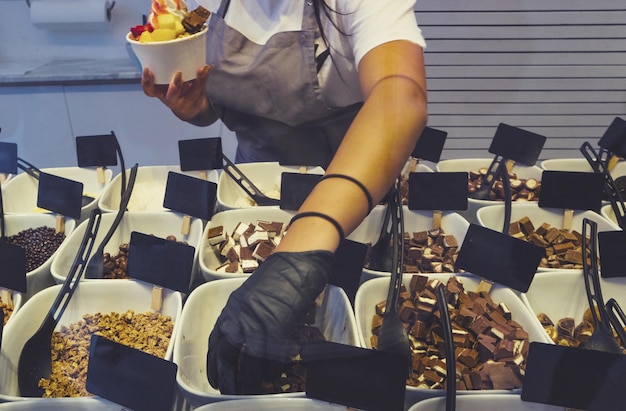 Foto el vendedor vierte coberturas en un yogur helado suave en una taza blanca para llevar