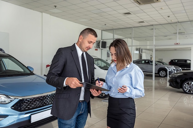 Foto vendedora caucásica que da consultas a un cliente masculino en una moderna y hermosa sala de exhibición de automóviles