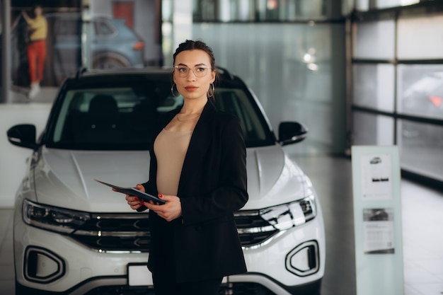 Vendedora con un clipboard cerca del coche en el concesionario