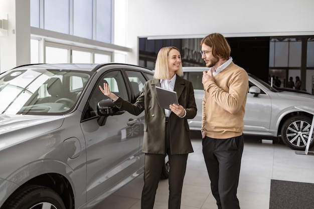 Foto una vendedora confiada explicando todas las características del coche usando una tableta al guapo dueño