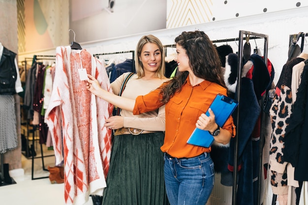 Vendedora feminina ajuda o comprador a escolher entre roupas diferentes.