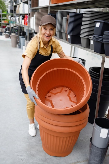 Vendedora feminina no centro de jardinagem move vasos de flores grandes e pesados