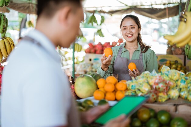 Vendedora de frutas revisando el sunkist mientras el vendedor masculino usa la tableta digital