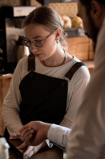 Vendedora jovem trabalhando em café ou cafeteria com dispositivo móvel e caixa registradora