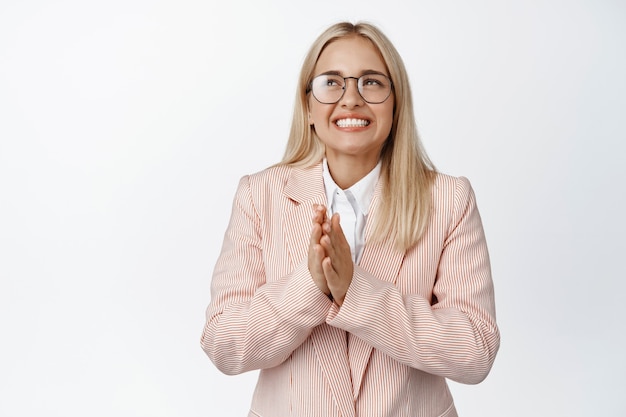 Vendedora joven esperanzada frotarse las manos, rezando por deleite, anticipando buenas noticias y sonriendo, de pie sobre blanco