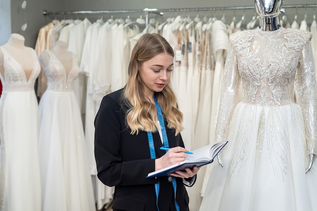 Vendedora sostiene bolígrafo y notas cerca del vestido de novia en la boutique