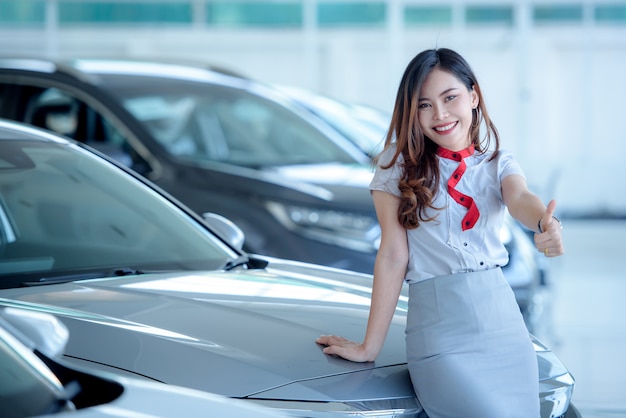 Los vendedores asiáticos hermosos están felices de vender autos nuevos en la sala de exposición y hacer que los clientes vengan a comprar autos en los concesionarios.